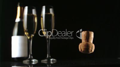 Champagne cork falling in front of  two glass flutes and bottle