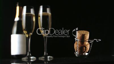 Champagne cork falling in front of  two glasses and bottle