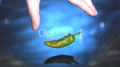 Jalapeno chili pepper being dropped into water by hand