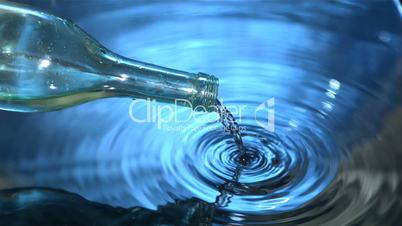 Glass bottle pouring water into blue water