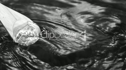 Oar moving through water with grass in black and white
