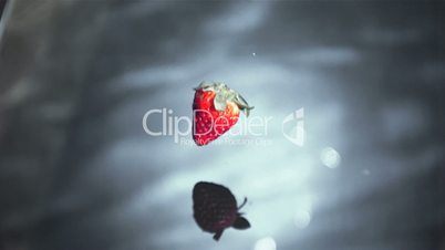 Strawberry falling into grey water