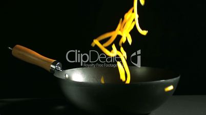 Sliced yellow pepper falling into wok on black background