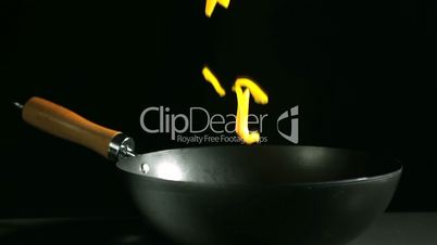 Sliced yellow peppers falling into wok on black background
