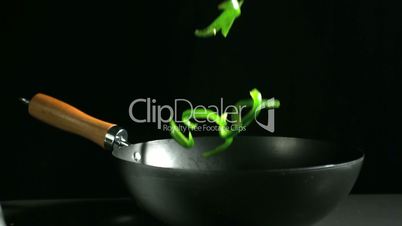 Sliced green peppers falling into wok on black background