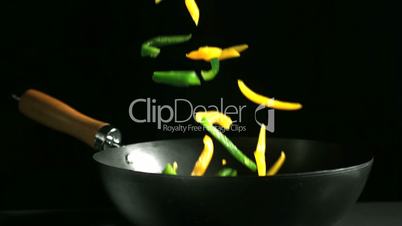 Mixed peppers falling into a wok on black background