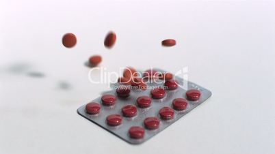 Red tablets falling onto blister pack on white background