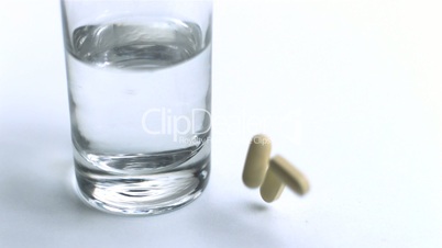 Pills falling beside glass of water