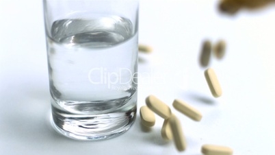 Large pills being poured out beside glass of water
