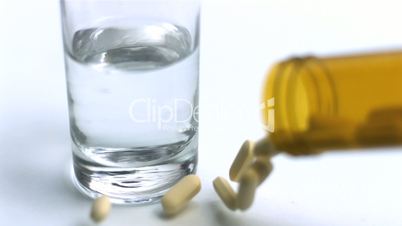 Pills pouring from jar beside glass of water