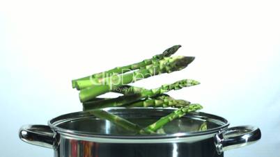 Many asparagus stalks falling into a saucepan