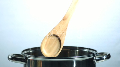 Wooden spoon falling into a saucepan