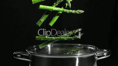 Asparagus falling in pot on black background