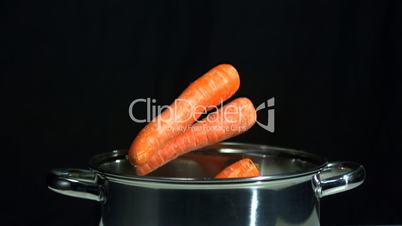 Carrots falling in saucepan on black background