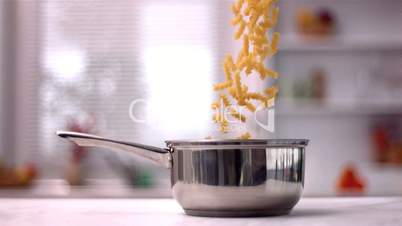 Fusilli falling in saucepan in kitchen