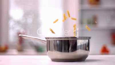 Fusilli falling into saucepan in kitchen