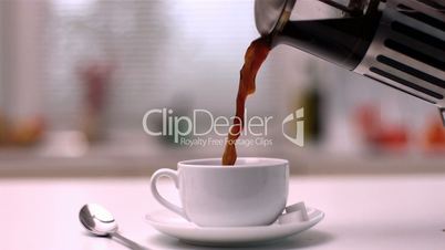 Coffee being poured from cafetiere into cup in kitchen