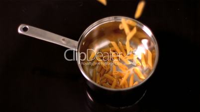 Penne falling into pot on black background