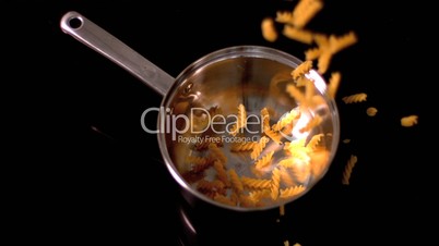 Fusilli falling into pot on black background