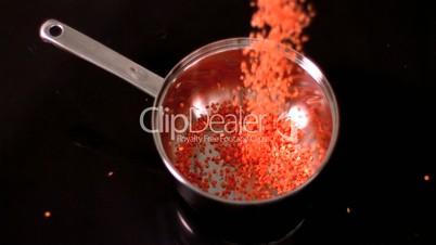 Red lentils falling into pot on black background