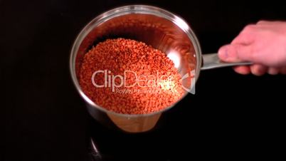 Man shaking red lentils in pot on black background