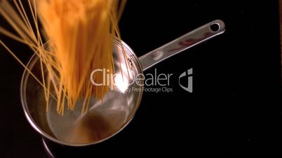 Spaghetti falling in a pot on black background