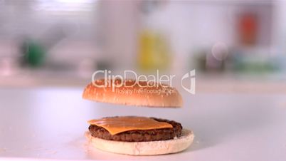 Bun falling on cheese burger in kitchen