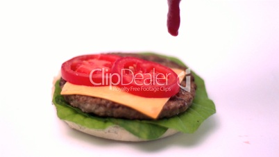 Ketchup pouring onto burger on white background