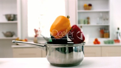 Red  green and yellow peppers falling in saucepan in kitchen