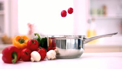 Cherry tomatoes falling in pot in kitchen beside vegetables