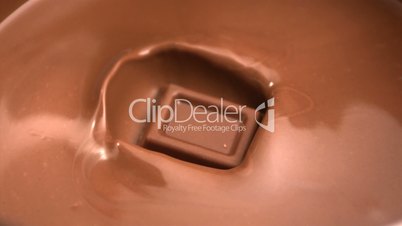 Square of chocolate falling into melted chocolate