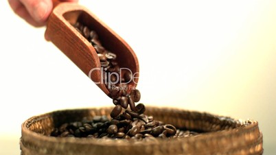 Coffee beans pouring from wooden scooper held by hand
