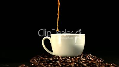 Coffee being poured into a cup on mound of coffee beans
