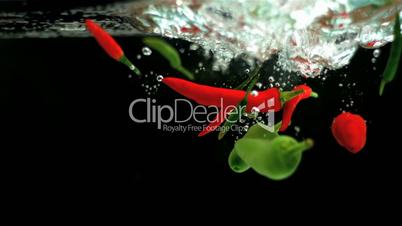 Red and green chili peppers falling in water