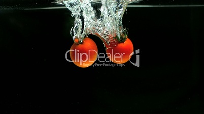 Two tomatoes falling in water