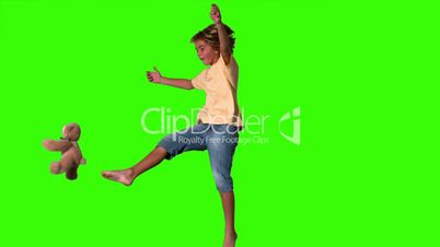 Boy jumping to kick teddy bear on green screen