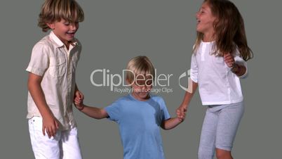 Siblings holding hands and jumping on grey background