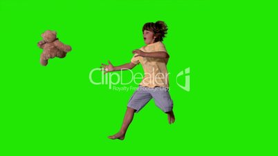 Young boy jumping up and catching teddy bear on a green screen