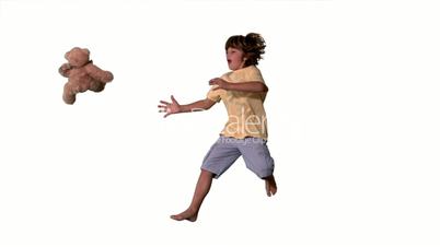 Young boy jumping up and catching teddy bear on a white background