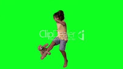Little boy jumping up and kicking teddy on a green screen