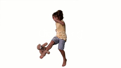 Little boy jumping up and kicking teddy on a white background