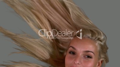 Attractive blonde tossing her hair up on grey background close up
