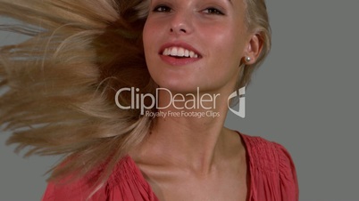 Attractive blonde shaking her hair up on grey background close up