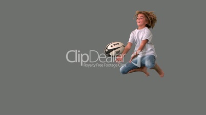 Boy jumping to catch rugby ball on grey background
