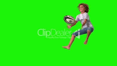 Boy jumping up to catch rugby ball on green screen