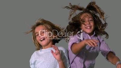Brother and sister jumping up and crashing on grey background