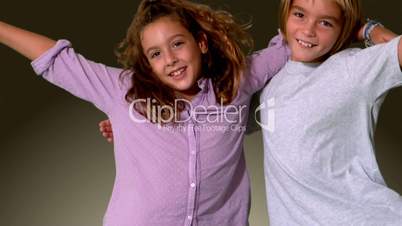 Brother and sister jumping into same shot and embracing on grey background