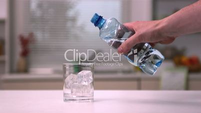 Hand pouring water into a glass with ice cubes