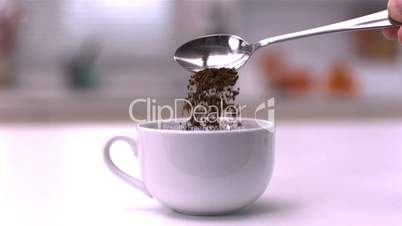 Pouring instant coffee from teaspoon into a white cup