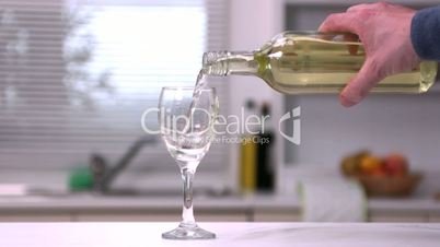 Mans hand pouring white wine from a bottle into a glass